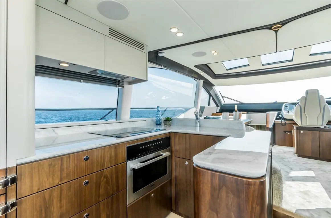 Modern yacht interior featuring a sleek kitchen with marble countertop, wooden cabinetry, and panoramic sea views.